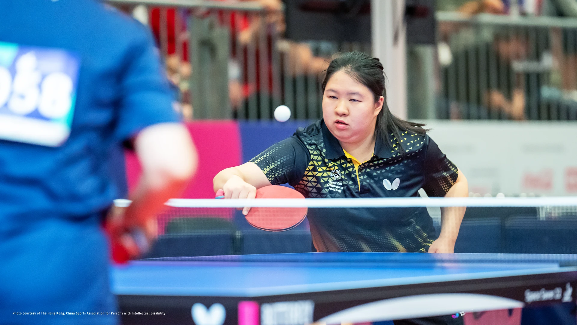 A man in a table tennis uniform striking the ping pong ball.